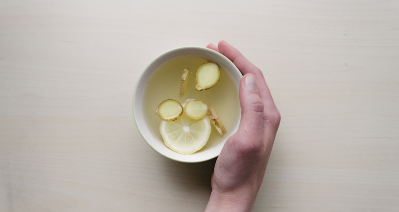 person holding white bowl with sliced lime and ginger inside