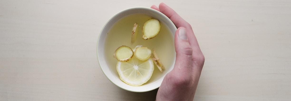 person holding white bowl with sliced lime and ginger inside