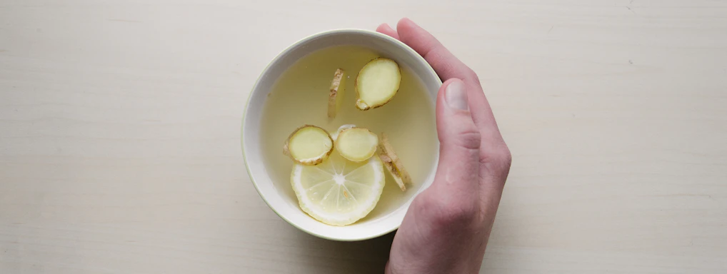 person holding white bowl with sliced lime and ginger inside
