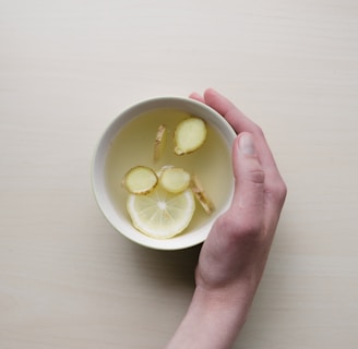 person holding white bowl with sliced lime and ginger inside