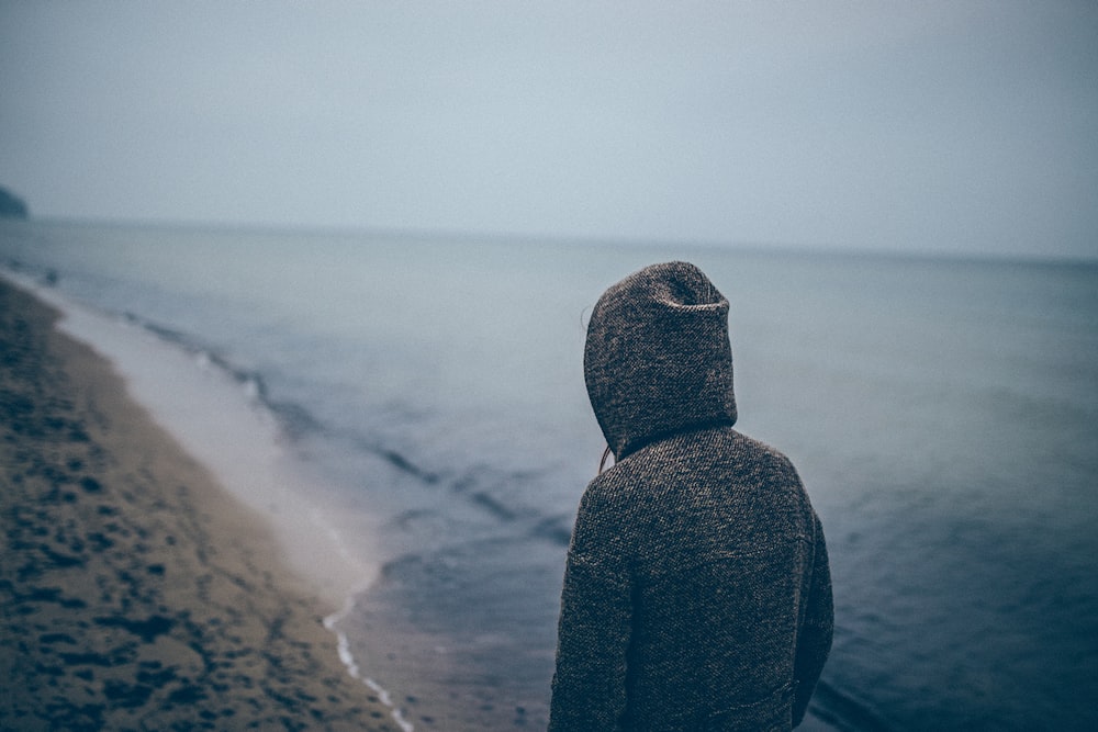 Person in a hoodie on a sandy beach filled with footprints