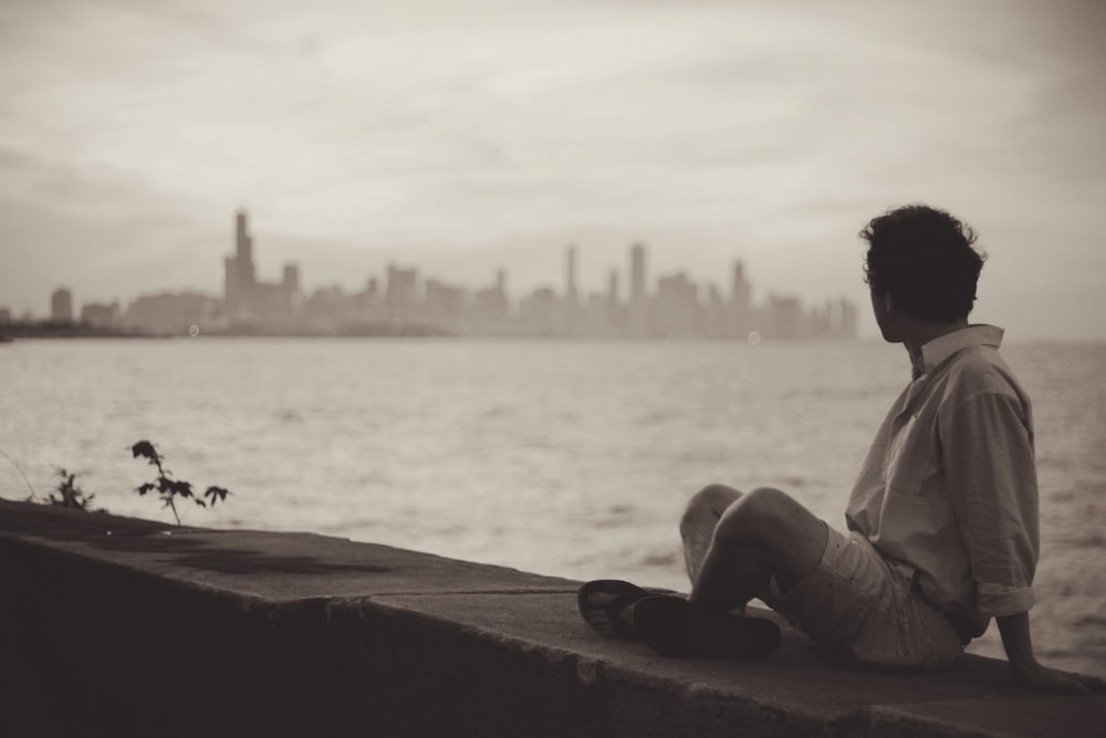 man beside body of water looking toward buildings