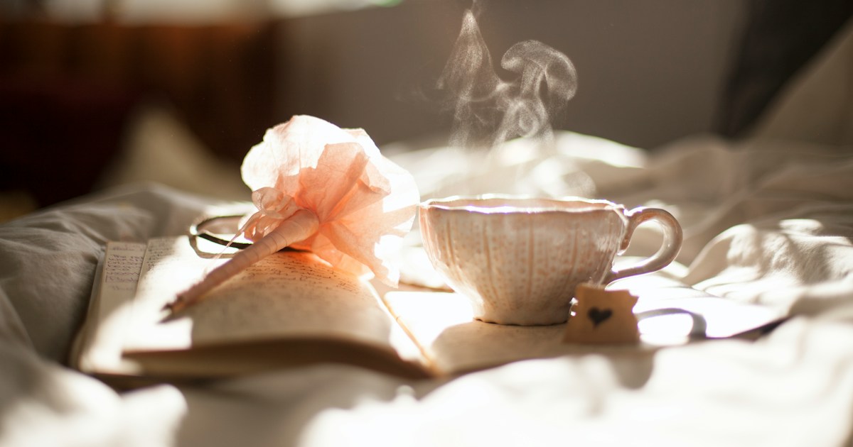 Ceramic teacup by Positive Quotes teacup on book beside pink flower decor