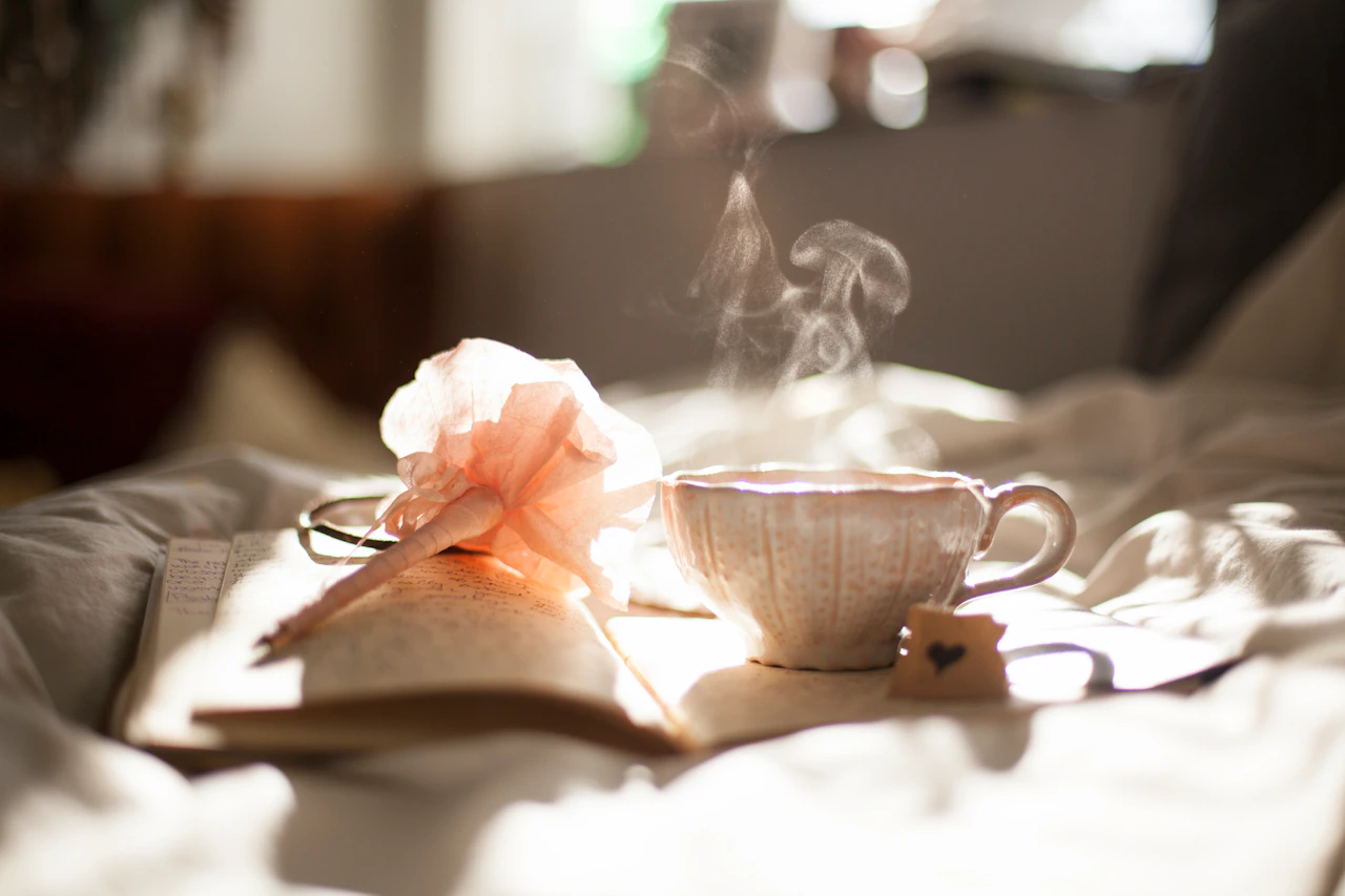 Dampfende Kaffeetasse und Lesebrille auf einem offenen Buch.