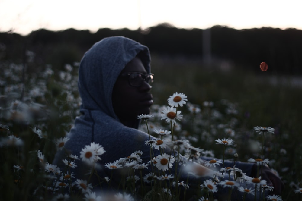 man wearing hoodie and surrounded by Daisy flowers