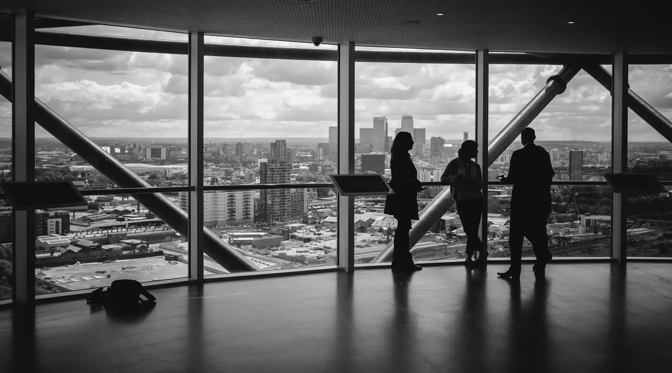 Consultores evaluando auditoría de blanqueo de capitales Tres profesionales conversando frente a una ventana panorámica con vista a una ciudad, representando un análisis estratégico en el contexto de una auditoría de blanqueo de capitales.