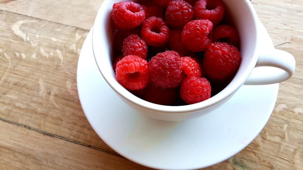 A coffee cup of raspberries on a saucer