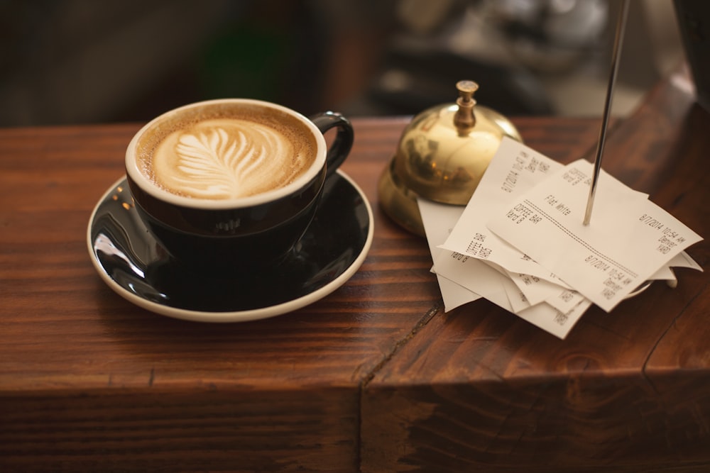 Taza de cerámica negra con platillo y capuchino sobre superficie de madera marrón