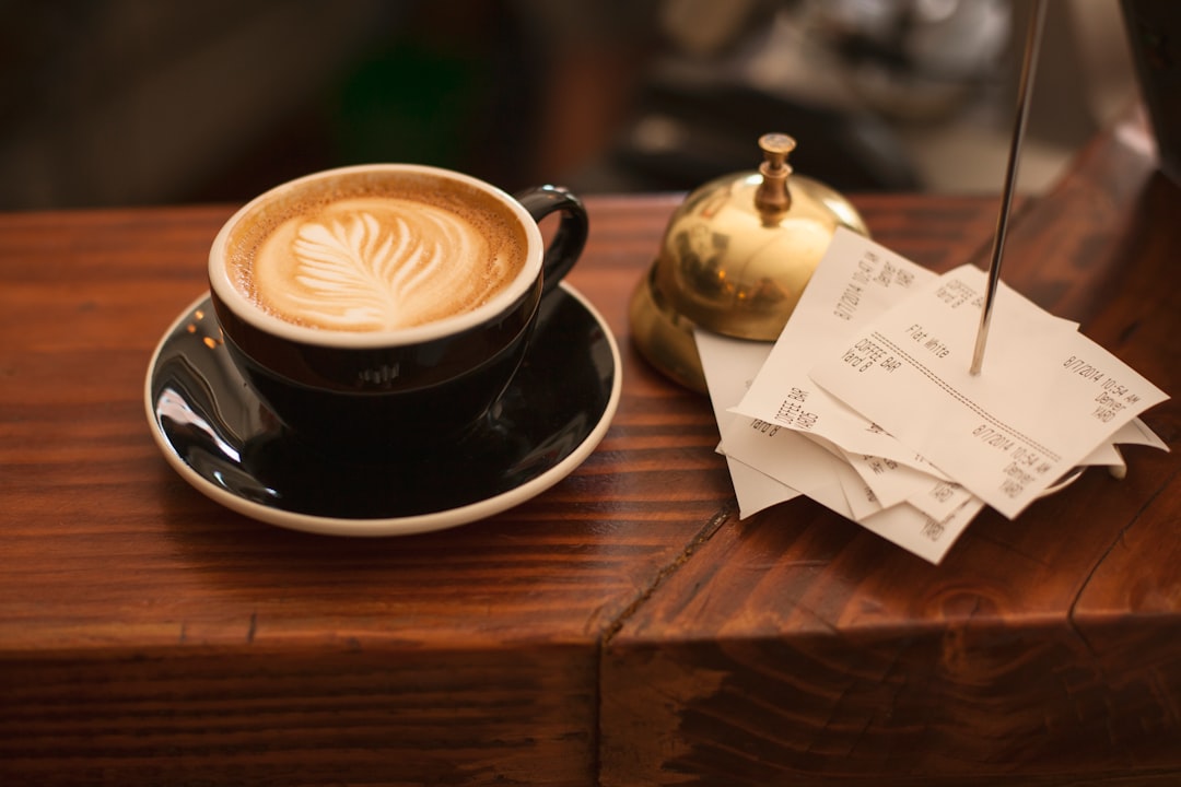 black ceramic cup with saucer and cappuccino on brown wooden surface