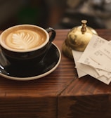 black ceramic cup with saucer and cappuccino on brown wooden surface