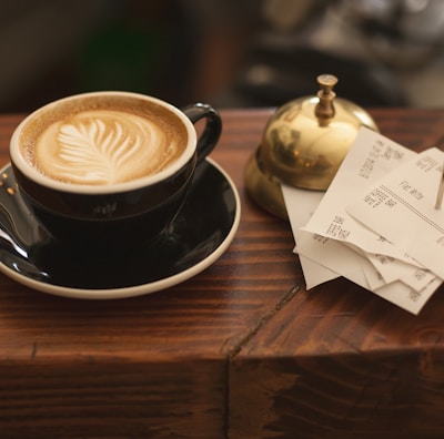 black ceramic cup with saucer and cappuccino on brown wooden surface