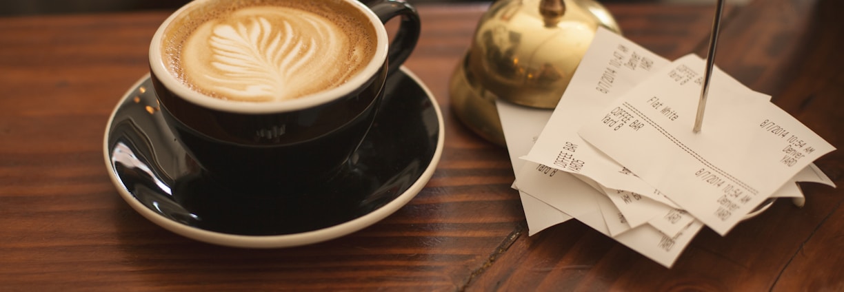 black ceramic cup with saucer and cappuccino on brown wooden surface