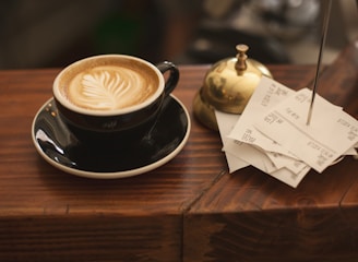 black ceramic cup with saucer and cappuccino on brown wooden surface