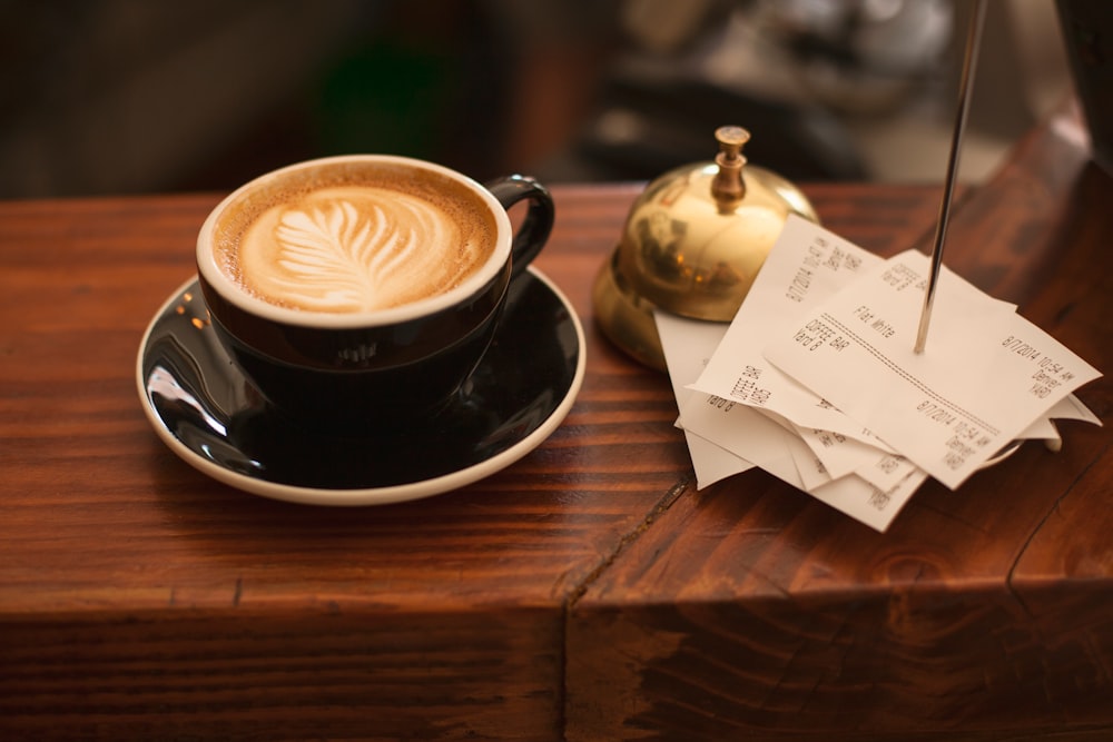 black ceramic cup with saucer and cappuccino on brown wooden surface