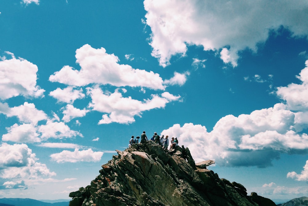 people on rock formation under white cloudy sky