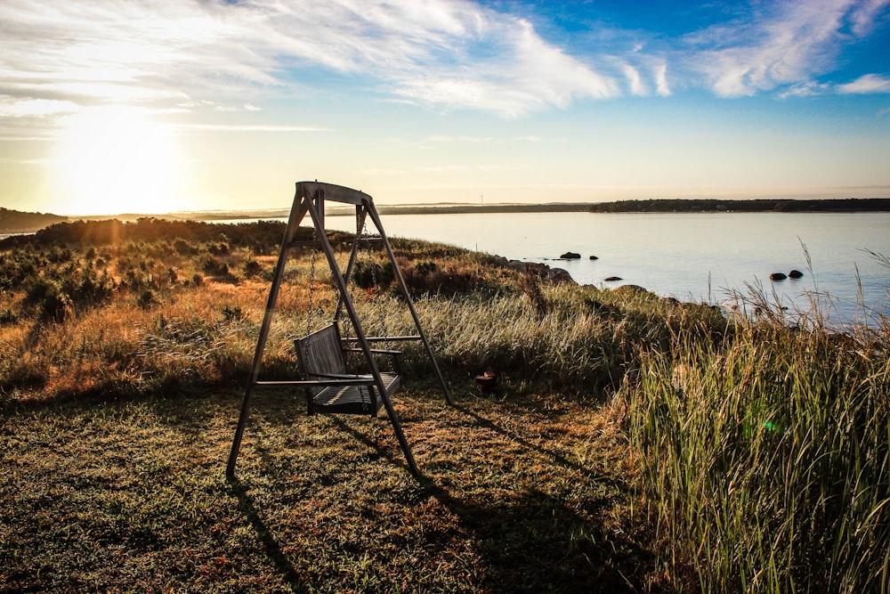 gray wooden bench swing facing body of water surrounded by grass