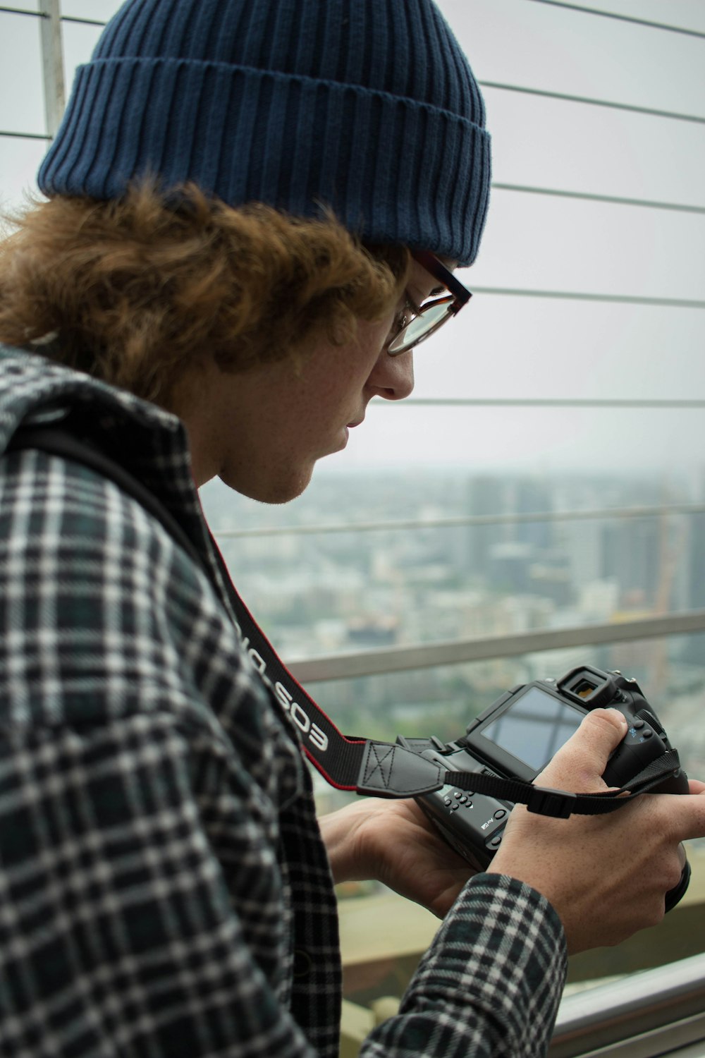 man in blue and white plaid shirt holding black dslr camera