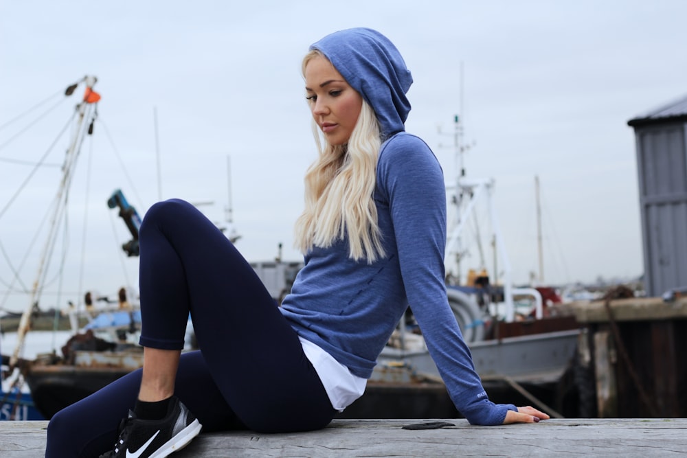 woman in blue hoodie and black leggings lounging at gray concrete surface