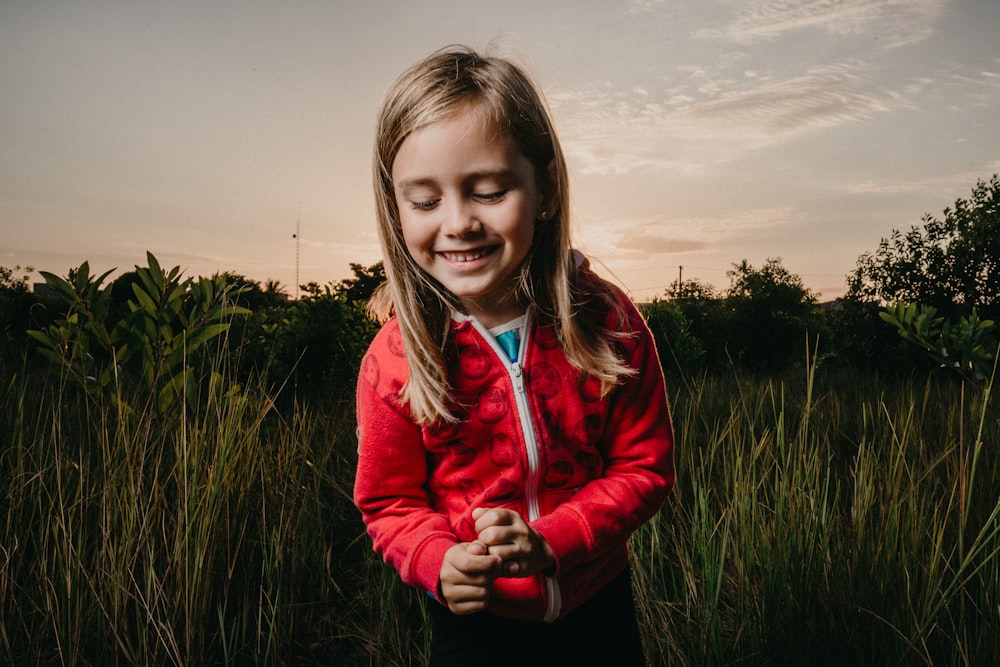 girl wearing red zip-up jacket standing on green grass