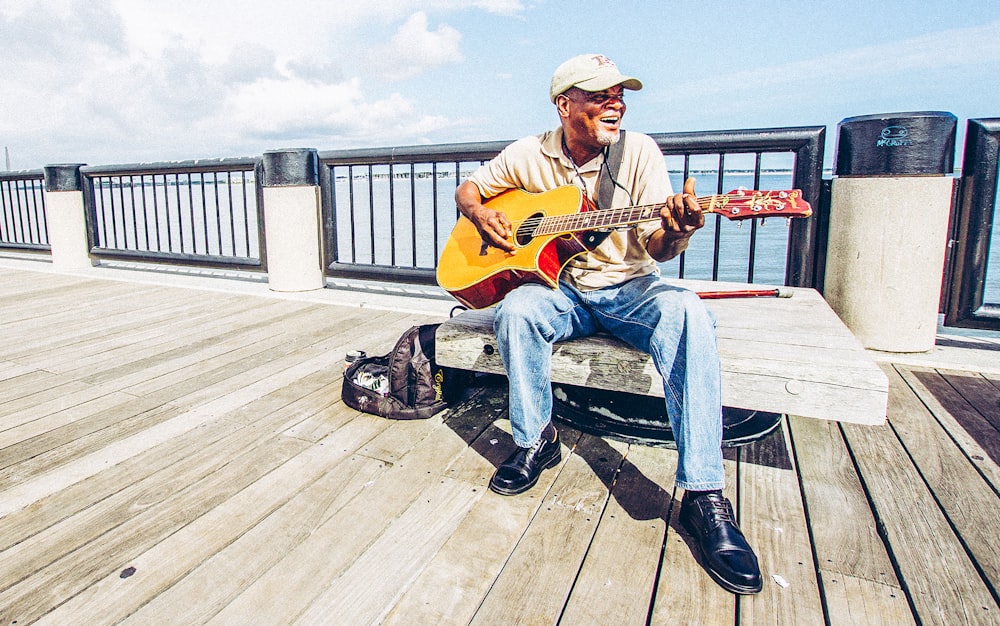 homme assis sur un banc tout en jouant de la guitare