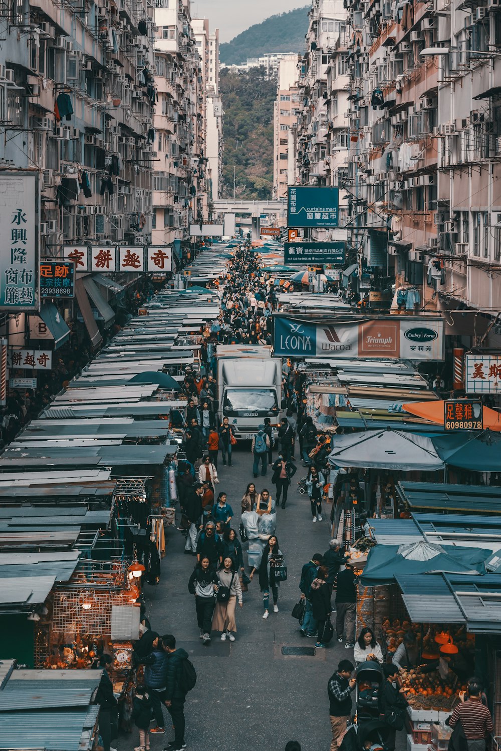 aerial photography of people walking past display stalls between concrete buildings during daytime