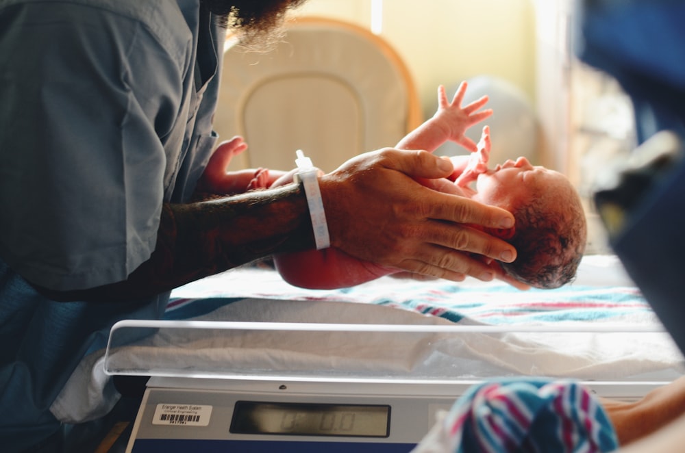 Person mit grauem Hemd legt Baby auf die Waage