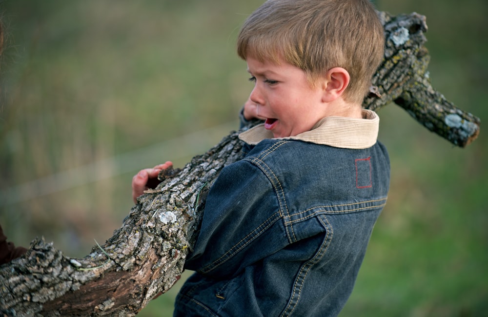 boy in blue denim jacket carrying dead tree branch