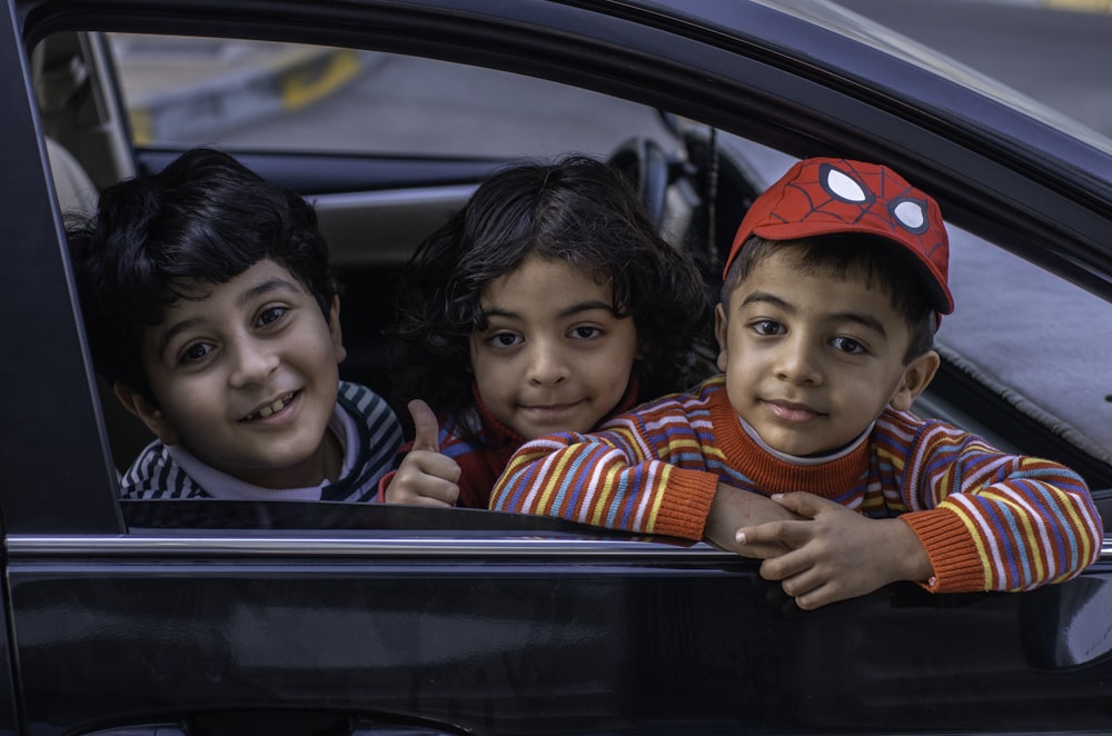 three boys looking outside window of car front seat