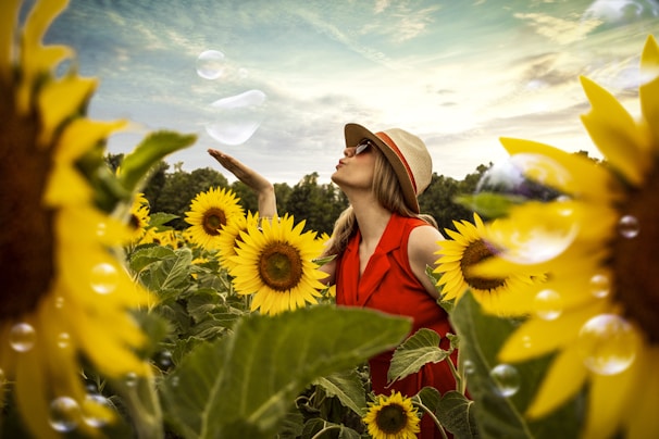 selective focus photography of woman blowing bubbles surrounded by sunflower field