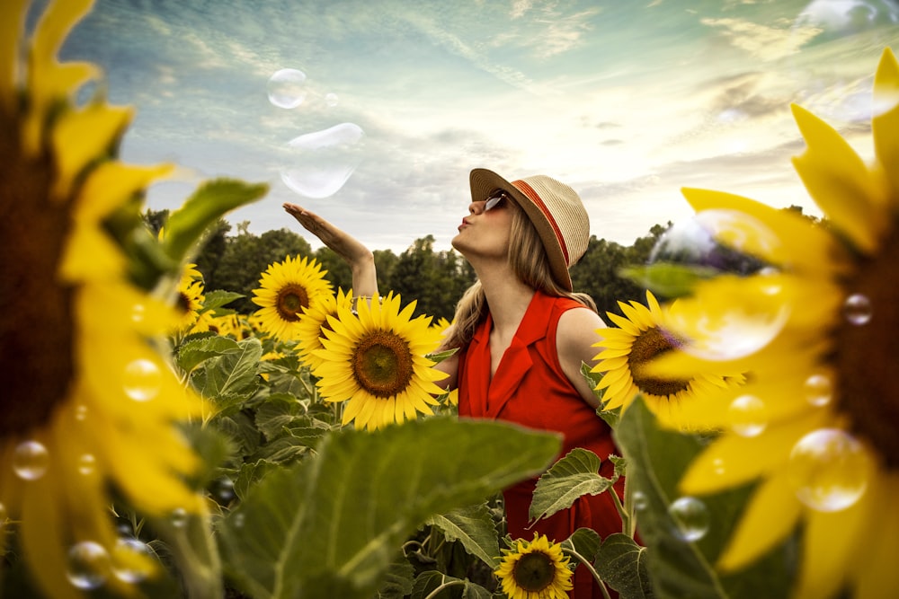 selective focus photography of woman blowing bubbles surrounded by sunflower field