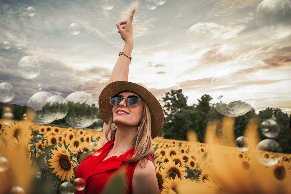 Mujer en la parte superior roja levantando la mano en el medio del campo de girasoles