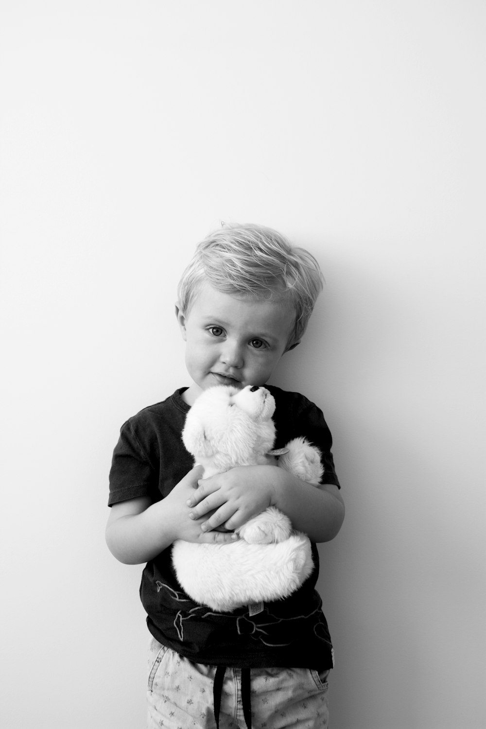 grayscale photography of boy holding bear plush toy