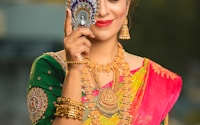 woman in green, gold, and red sari dress hiding her right eye while smiling