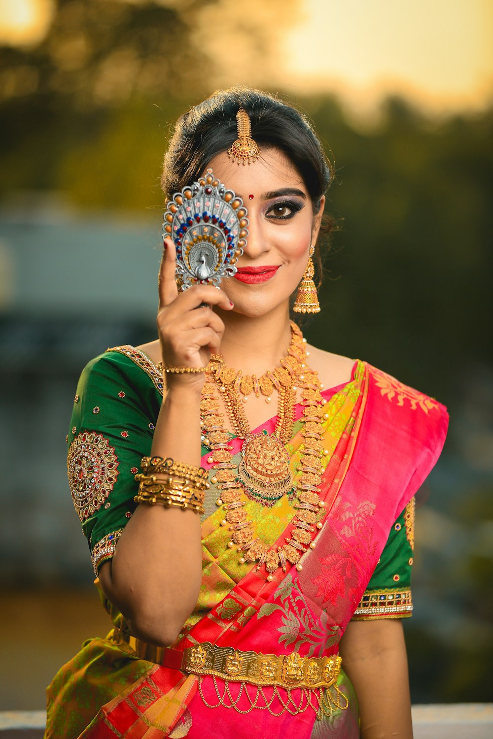 Mujer con vestido de sari verde, dorado y rojo que oculta su ojo derecho mientras sonríe
