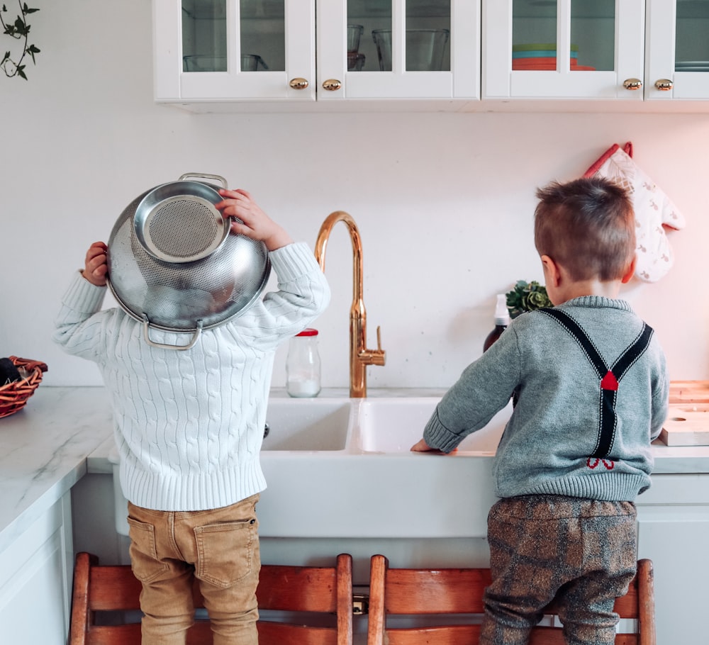 two boys standing on chair near sink