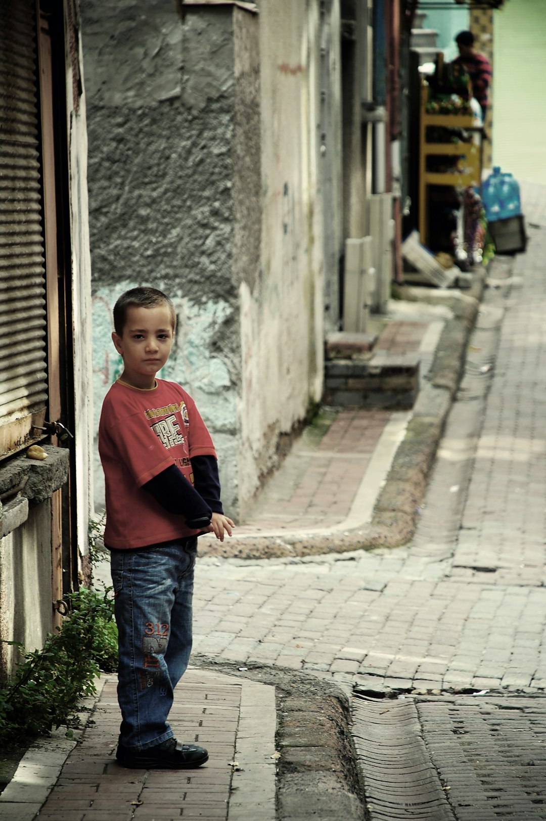 boy in red shirt standing by the street corner