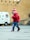 A young child wearing a colorful knit hat and a red sweater is walking across a paved area. The child seems to be holding a small object in their hand. In the background, there is a white van with medical symbols and some text. The setting appears to be an outdoor area with large, beige-colored walls.