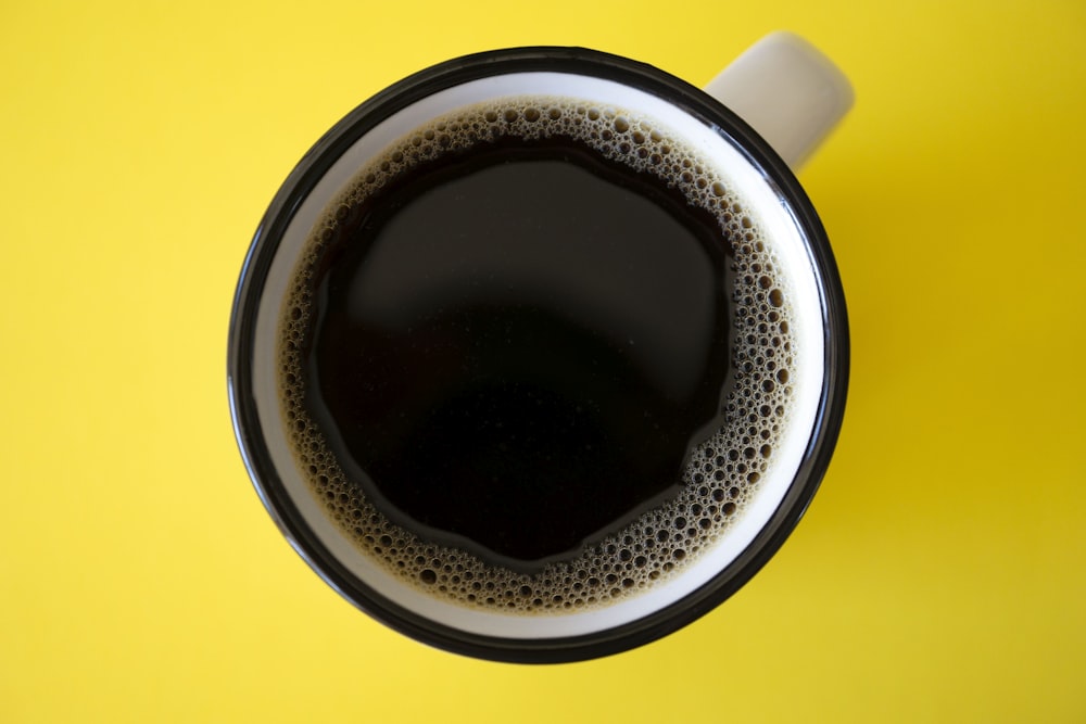taza de café negro sobre superficie amarilla