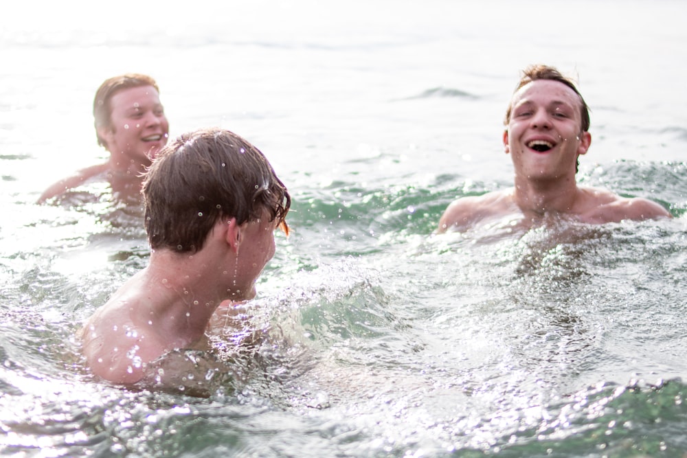 three men smiling while swimming during daytime
