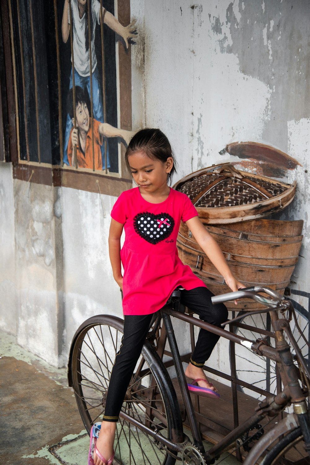 girl sitting on bicycle near wall during daytime