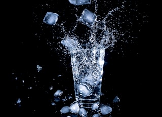 ice cubes dropped in clear drinking cup with water