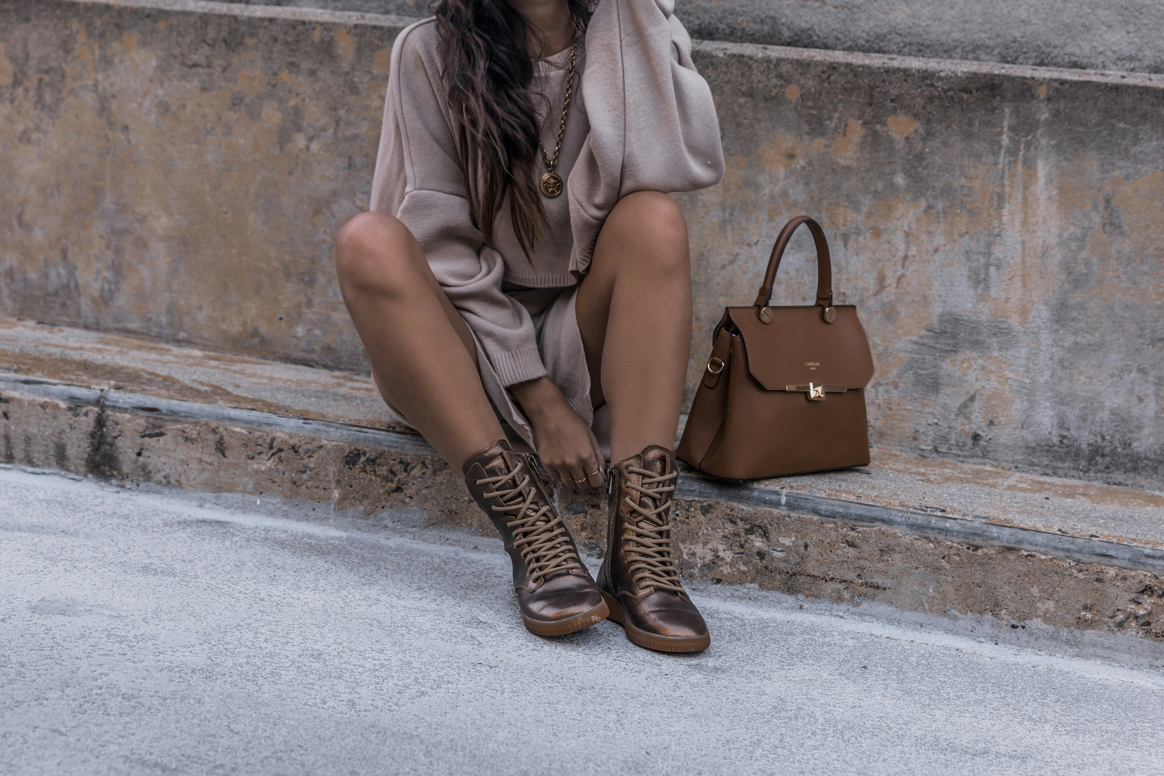 Please help support by following @dayinmydreams on Instagram xoxo Girl sits on a cement street curb wearing a sweater dress and metallic copper hiker boots with a luxury handbag. Neutral beige tones are great for overlaying white fonts or graphics.