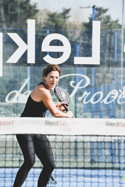 A close-up action shot of a senior woman hitting a precise backhand swipe in padel.