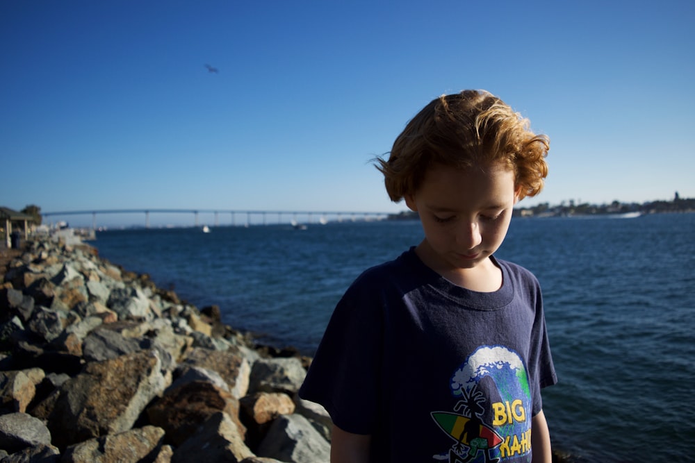 boy standing on rocking shore while looking down