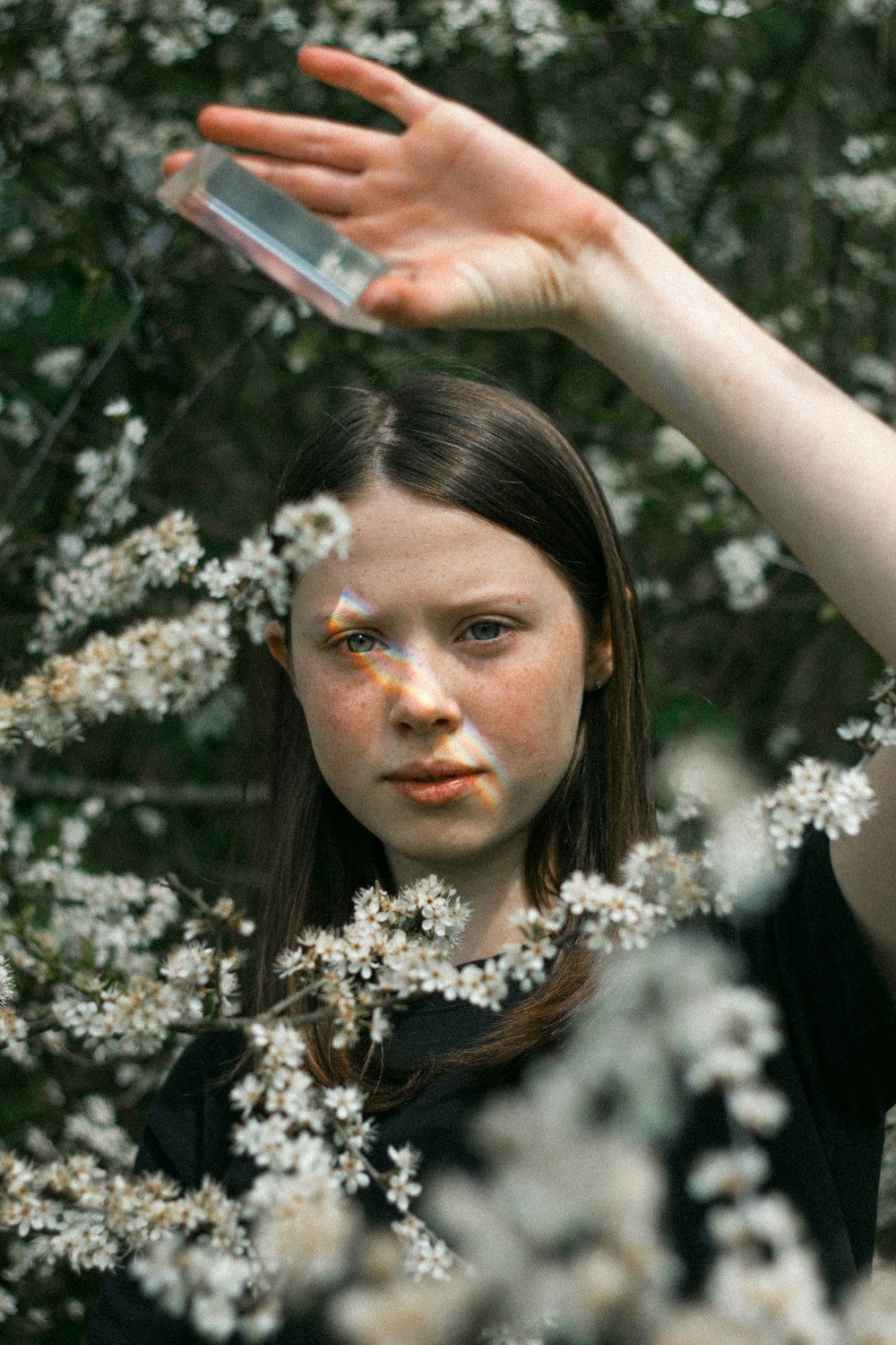 girl holding glass panel while standing behind white-flowering bush