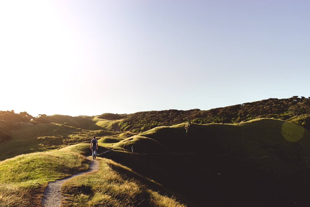 person walking on green hill at daytime