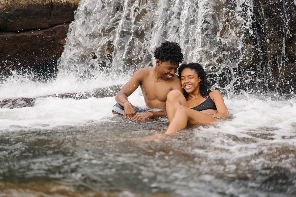 smiling topless man sitting near smiling woman beside waterfalls