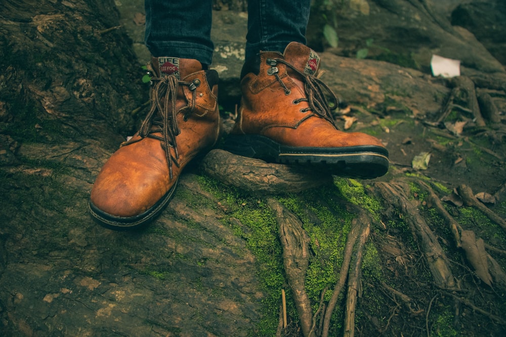 person in brown work boots on top of tree root