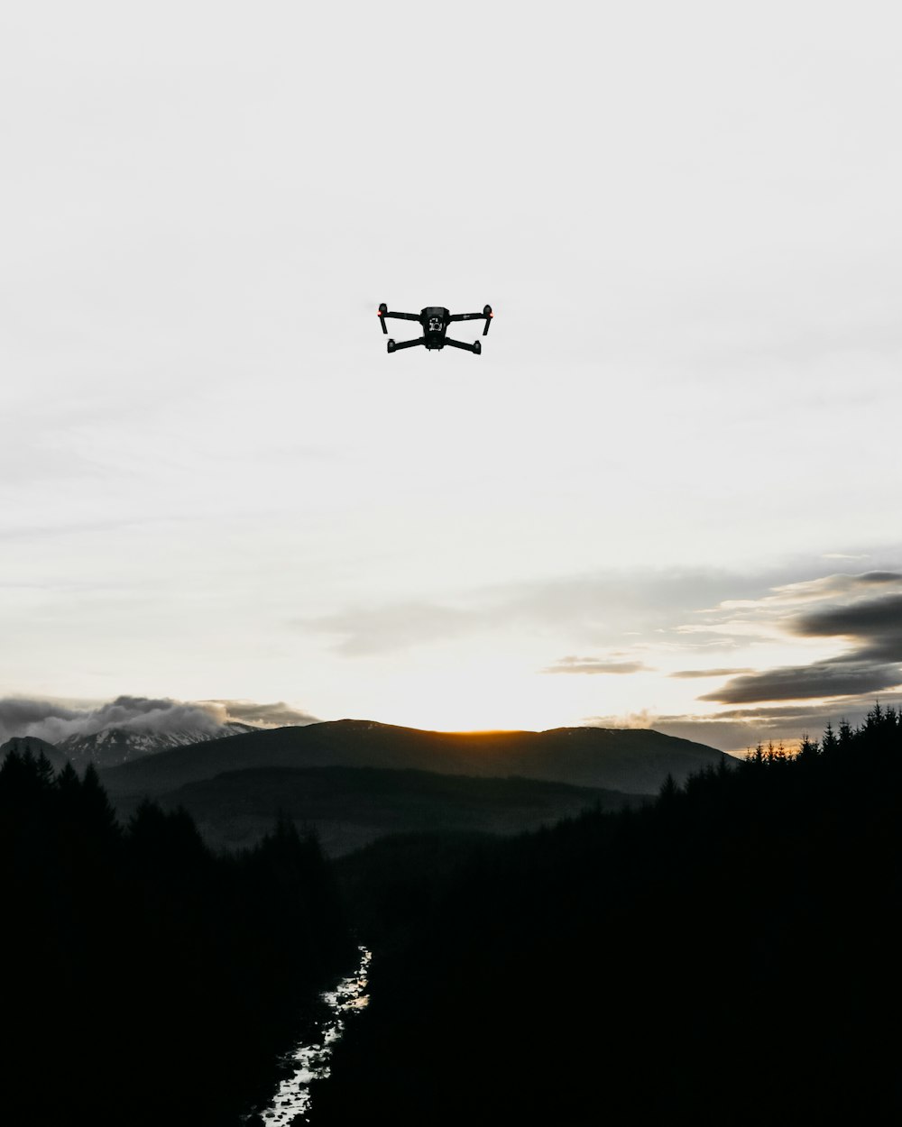 black quadcopter in the sky overlooking trees and mountain