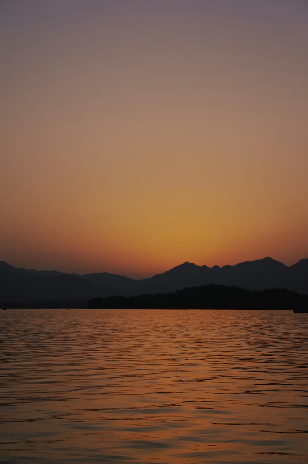 silhouette of mountain near calm sea during sunset